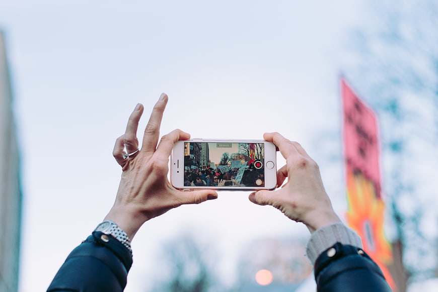 Hands holding smartphone recording protest crowd