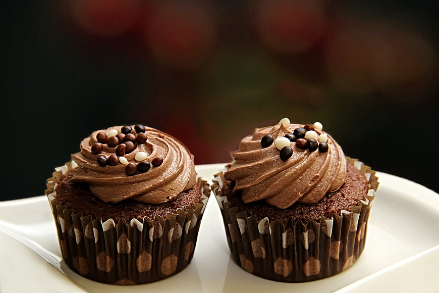 Two Chocolate Frosted Cupcakes With Chocolate Chips On White Plate