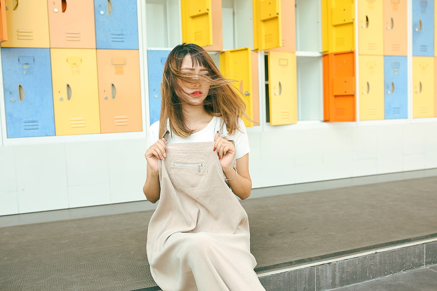 Young woman with windblown hair sitting in front of colorful lockers
