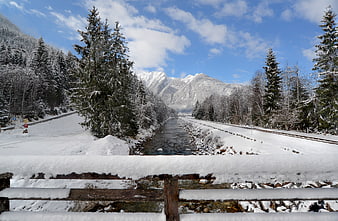 Snowy winter landscape with river, mountains, and train tracks