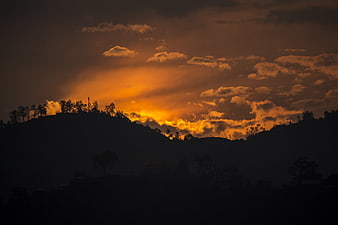Dramatic Orange Sunset Over Silhouetted Hills And Clouds
