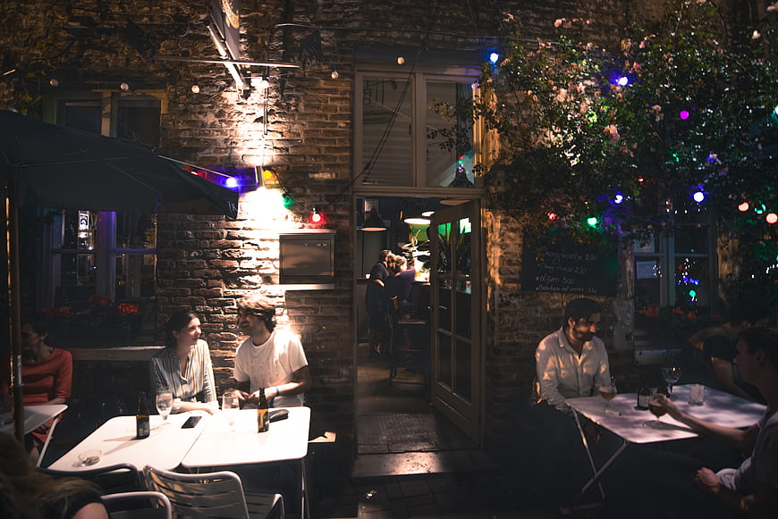 People dining at outdoor cafe at night with string lights