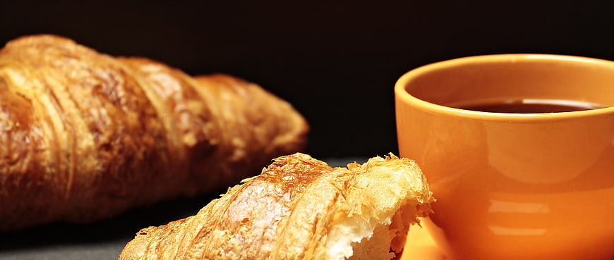 Golden Croissant and Orange Coffee Cup on Dark Background