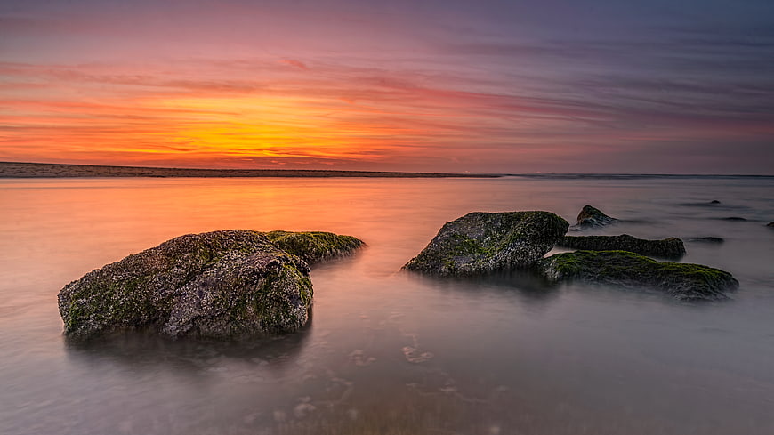 Long Exposure Sunset Over Mossy Rocks on Calm Beach