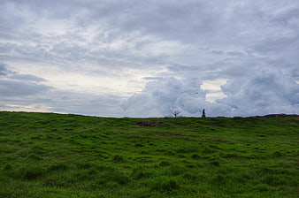 Woman Silhouette on Green Hill Under Dramatic Clouds
