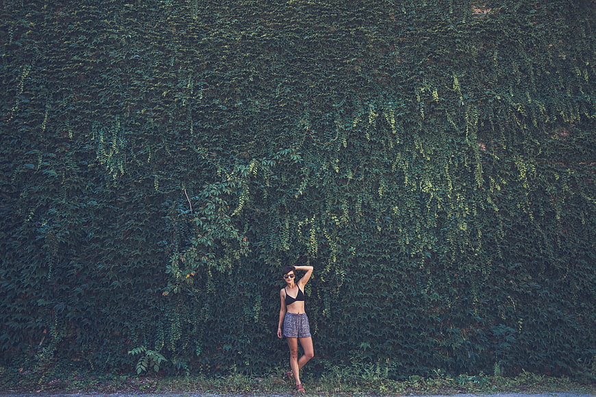 Woman in Black Bikini Top Standing Against Green Ivy Wall