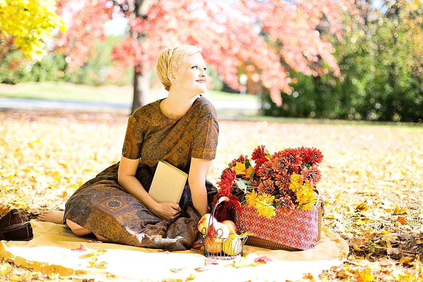 Woman reading book on autumn picnic blanket with flowers