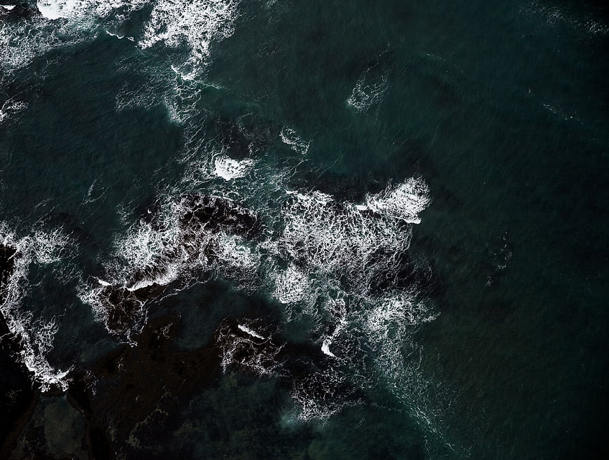 Aerial View of Dark Ocean Waves Crashing on Rocks