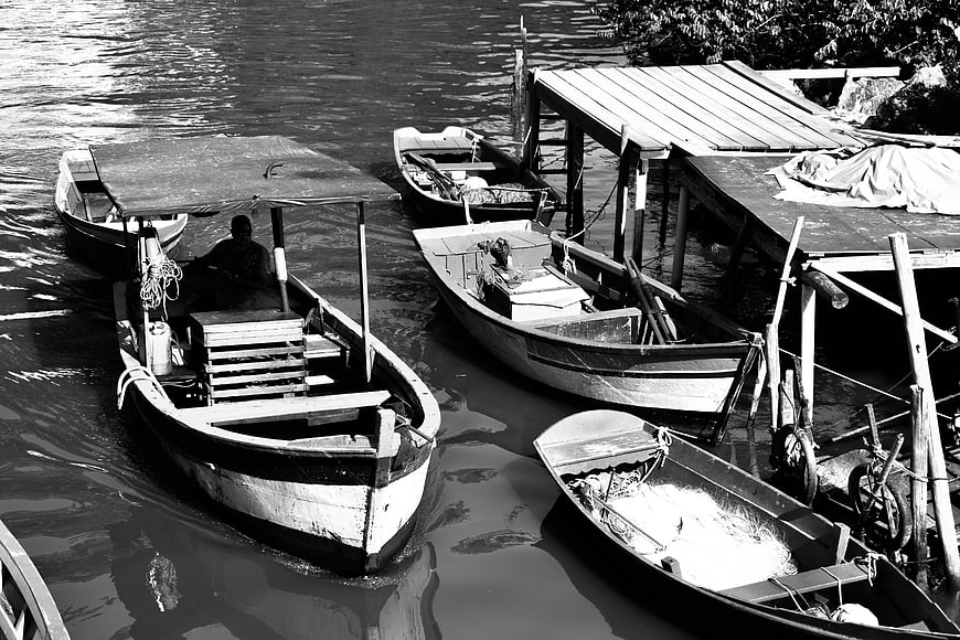 Black and white photo of wooden fishing boats docked at a riverside pier