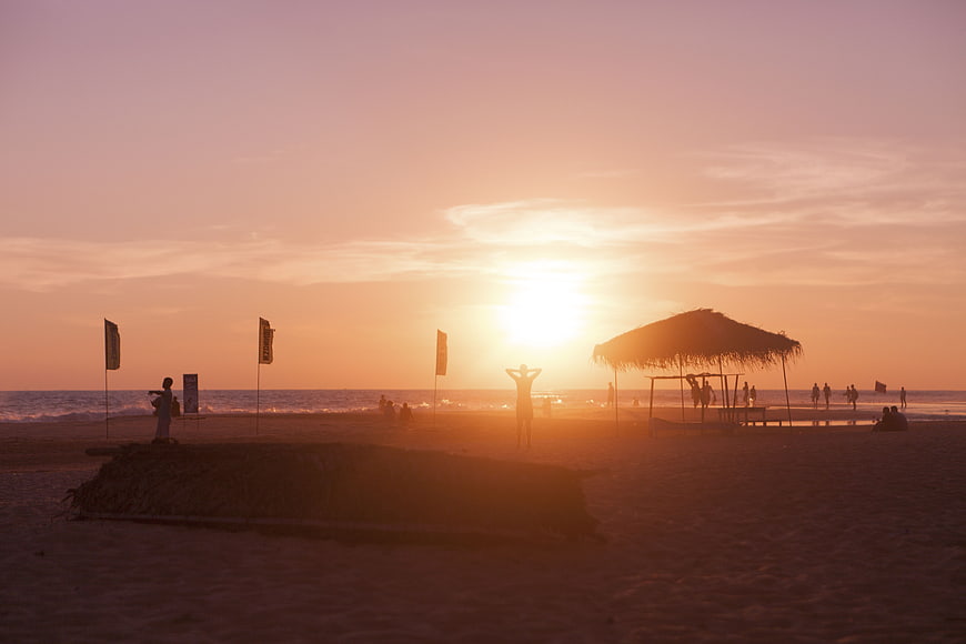 Silhouetted Beach Sunset with Thatched Hut and Ocean Waves