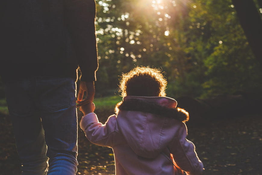 Father and Child Walking Hand in Hand in Sunlit Forest