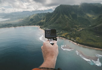 Hand holding action camera over tropical coastline and mountains