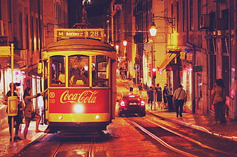 Vintage yellow tram with Coca-Cola branding on a narrow street in Lisbon at night