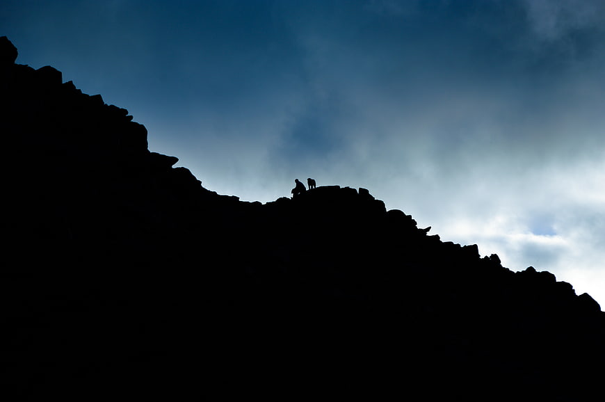 Silhouette of Hikers on Mountain Ridge Against Blue Sky