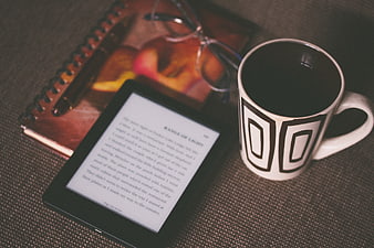 E-reader, coffee mug, and notebook on textured surface