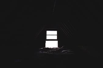 Dark attic bedroom with bright window and unmade bed