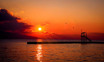 Vibrant Orange Sunset Over Ocean With Silhouetted Pier