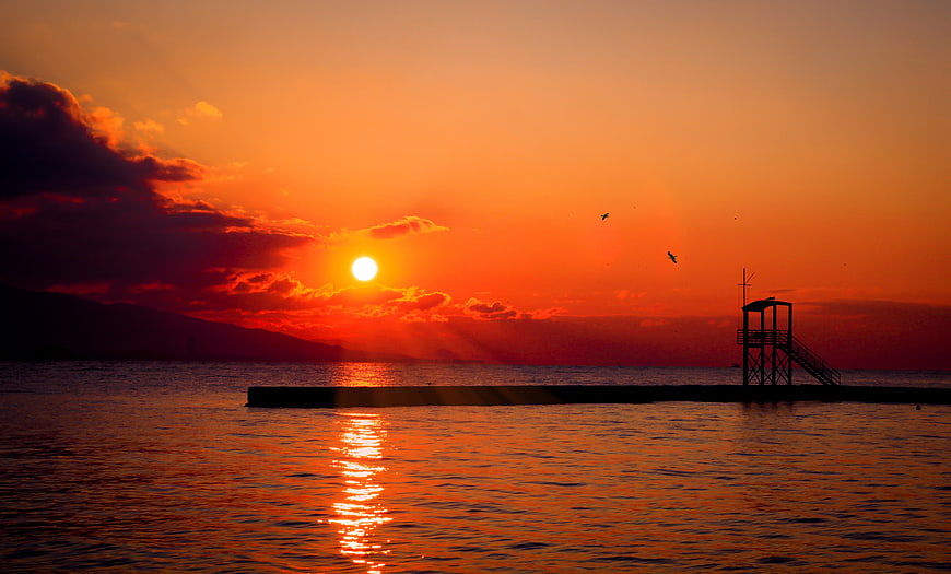 Vibrant Orange Sunset Over Ocean With Silhouetted Pier