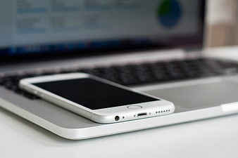 White smartphone resting on silver laptop keyboard close-up