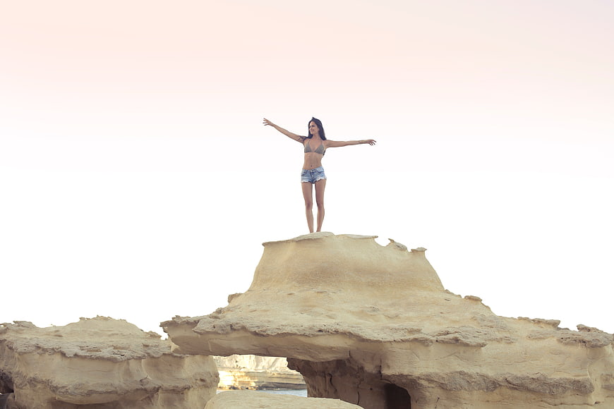 Woman standing on rock formation with arms outstretched