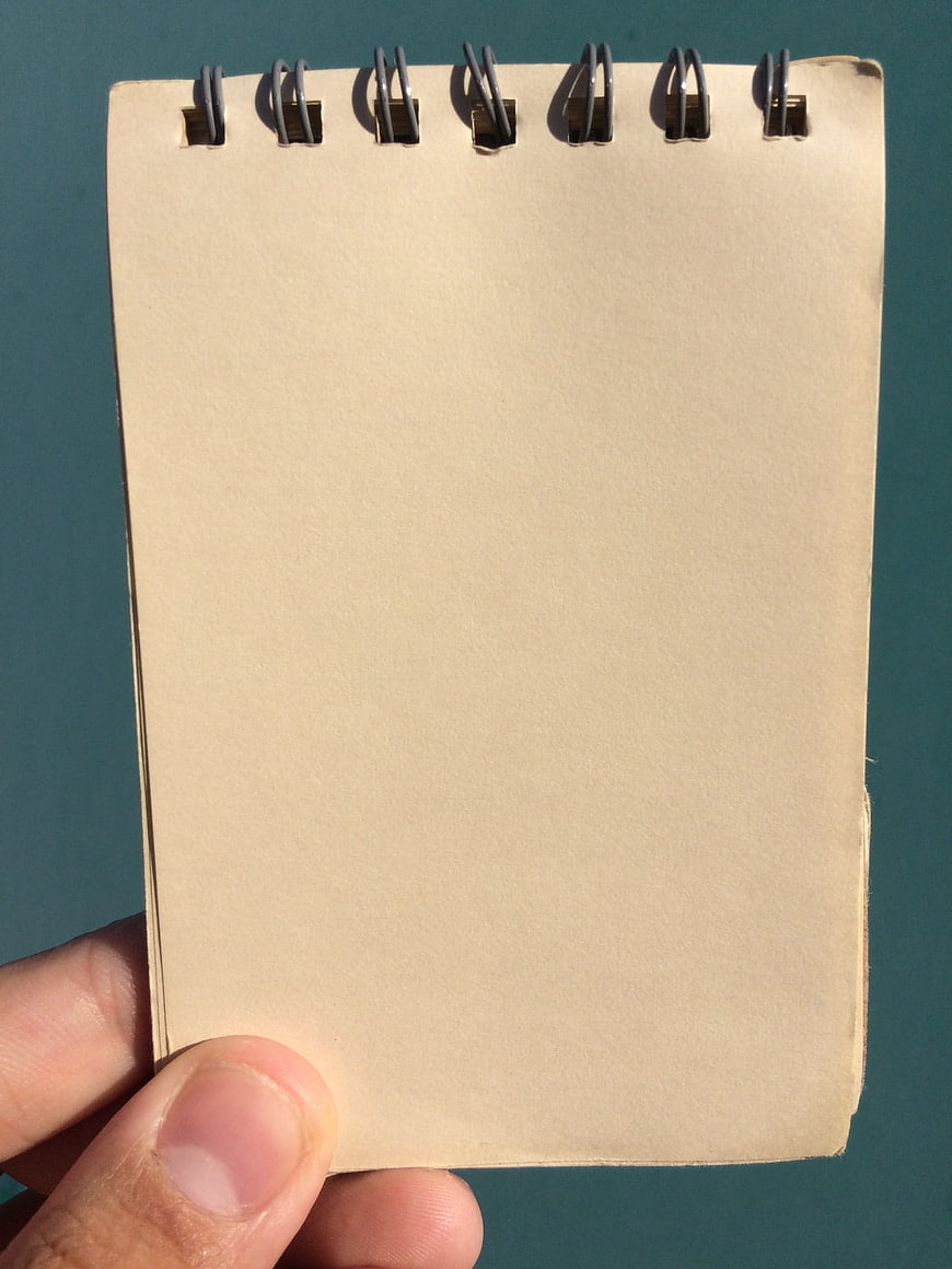 Hand holding blank spiral notepad against teal background