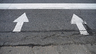 Worn white directional arrows painted on cracked asphalt road surface