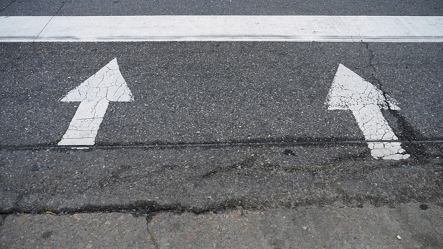 Worn white directional arrows painted on cracked asphalt road surface