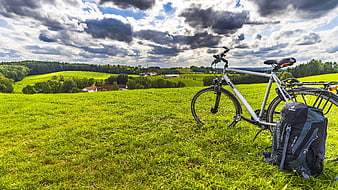 Bicycle and Backpack in Green Meadow with Dramatic Clouds
