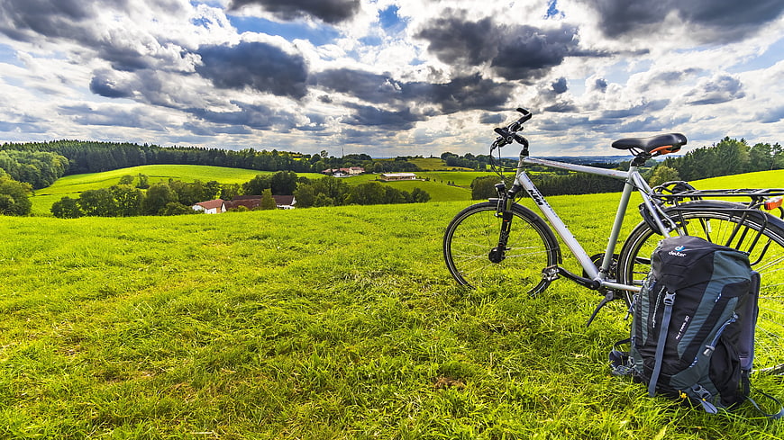 Bicycle and Backpack in Green Meadow with Dramatic Clouds