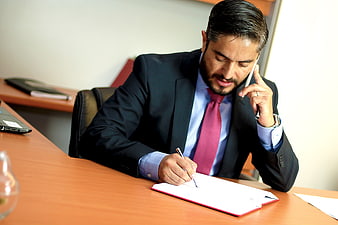Businessman in suit writing notes while talking on phone