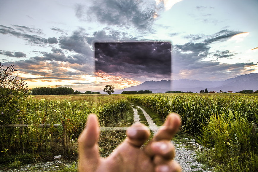 Hand holding transparent glass pane over rural cornfield landscape