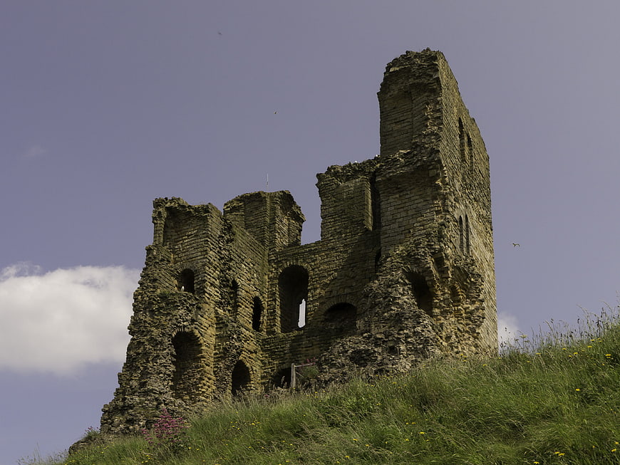 Ancient stone castle ruins on a grassy hill against a cloudy sky