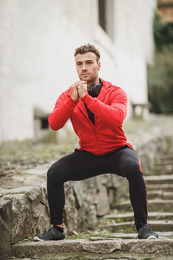 Athletic man in red hoodie performing squat exercise outdoors