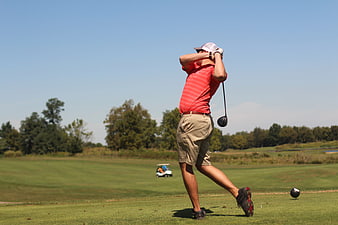 Golfer swinging club on sunny green course