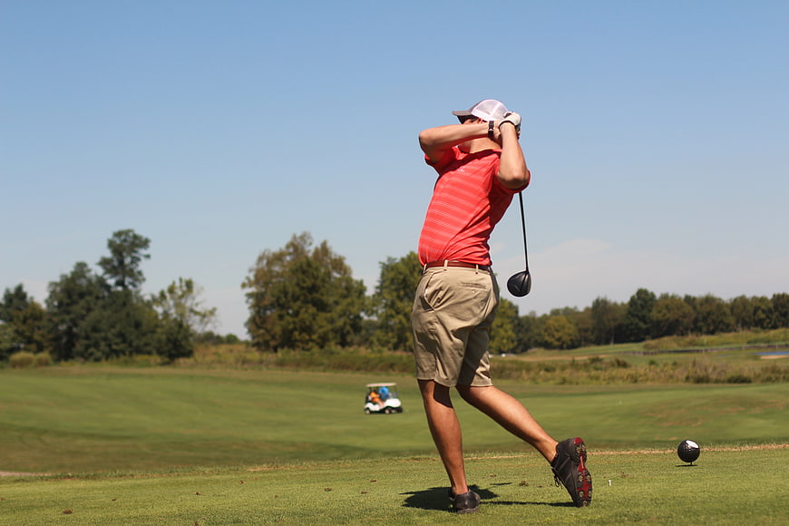 Golfer swinging club on sunny green course