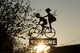 Silhouette of children on bicycle welcome sign at sunset