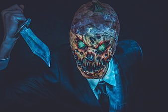 Scary man in suit with pumpkin mask holding knife