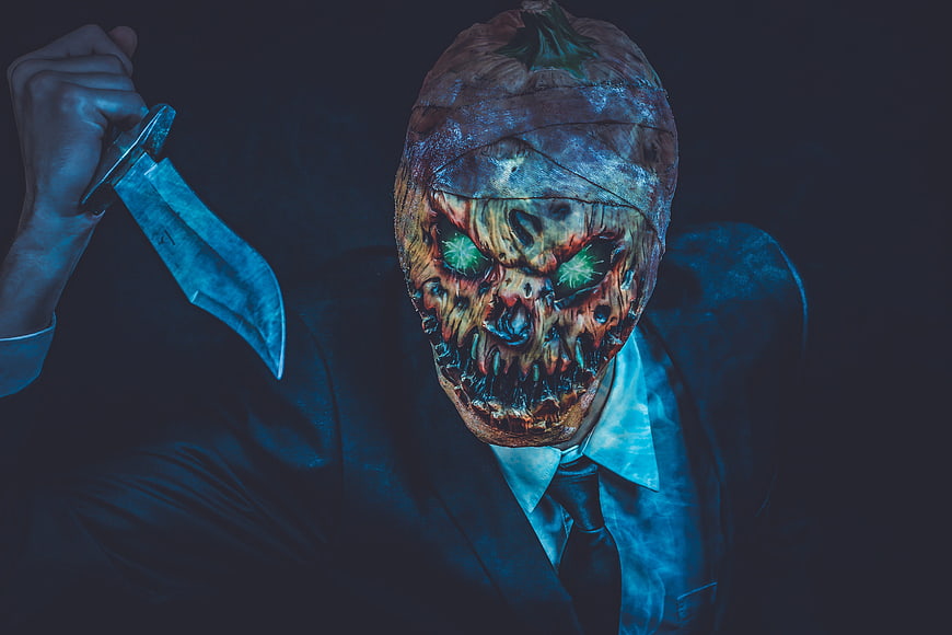 Scary man in suit with pumpkin mask holding knife