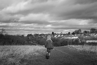 Child walking away with sticks in black and white landscape