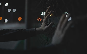 Hands touching chain link fence at night with bokeh lights