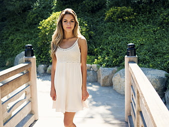 Young woman in white summer dress standing on wooden bridge
