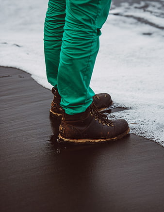 Close-up of brown leather boots on wet beach with foam