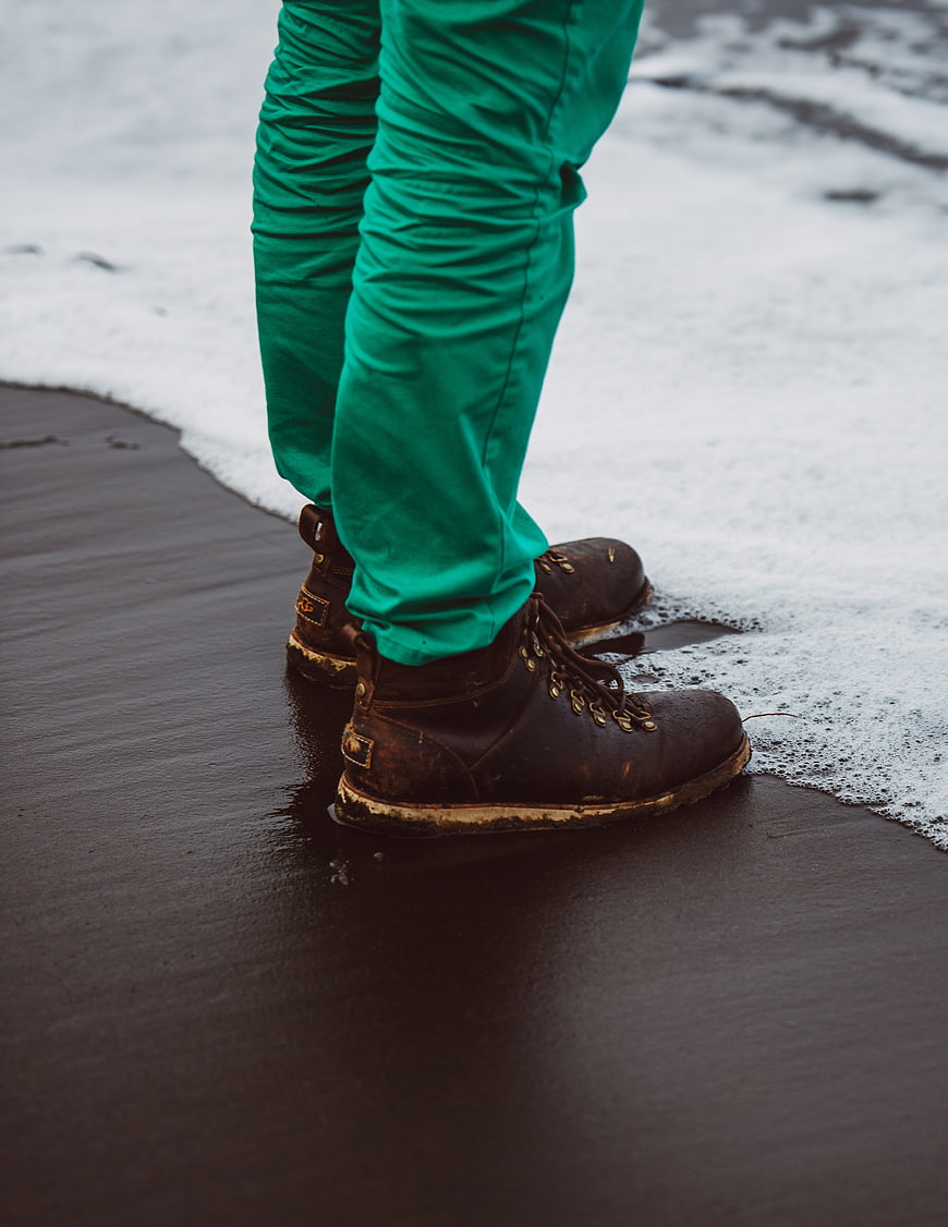 Close-up of brown leather boots on wet beach with foam