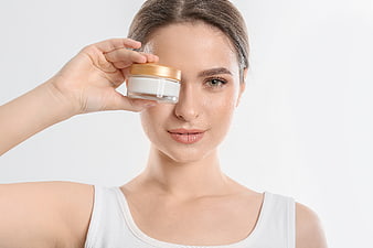 Woman holding skincare cream jar over eye