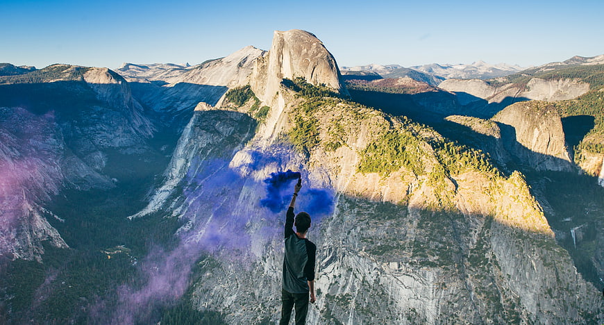 Man Throwing Blue Smoke Bomb on Mountain Cliff Edge