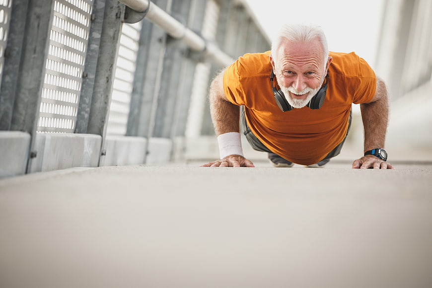 Senior man doing push-ups on bridge with headphones