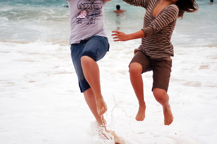 Two friends jumping in ocean waves at the beach