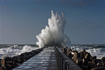 Dramatic ocean wave crashing against a wooden pier in a storm