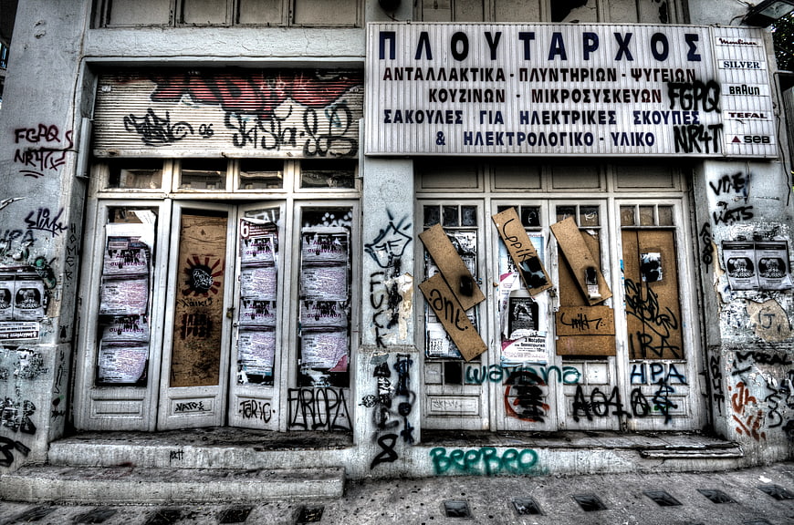 Abandoned Greek storefront with graffiti and boarded windows