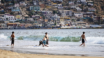 Boys playing in ocean waves with colorful hillside town background
